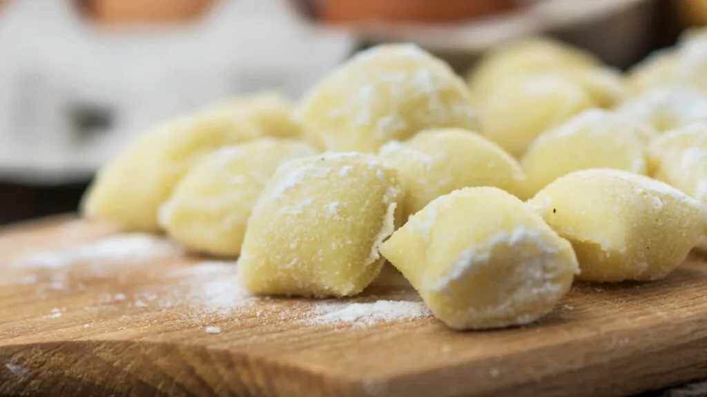 Pile of soft potato gnocchi dusted with flour on a wooden board