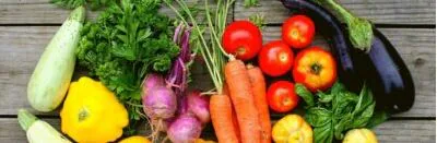 Fresh spring vegetables including squash, carrots, radishes, tomatoes, eggplant and basil on wood
