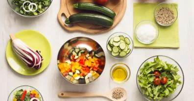 Overhead view of chopped vegetables, salads, zucchini and seeds laid out on a white table
