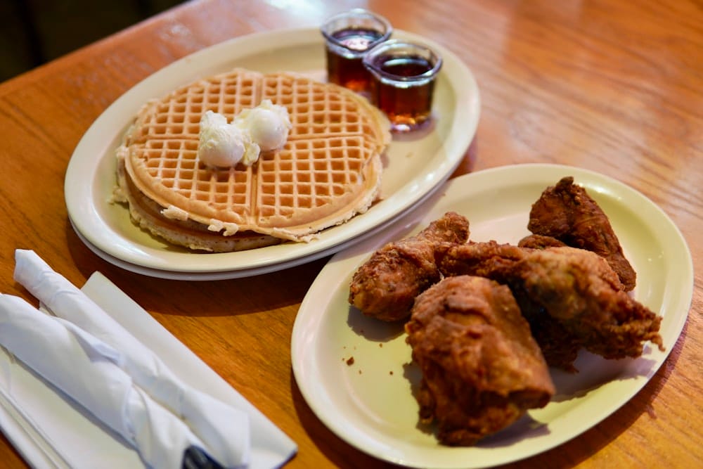 Plate of golden waffles with butter next to fried chicken and small pitchers of syrup