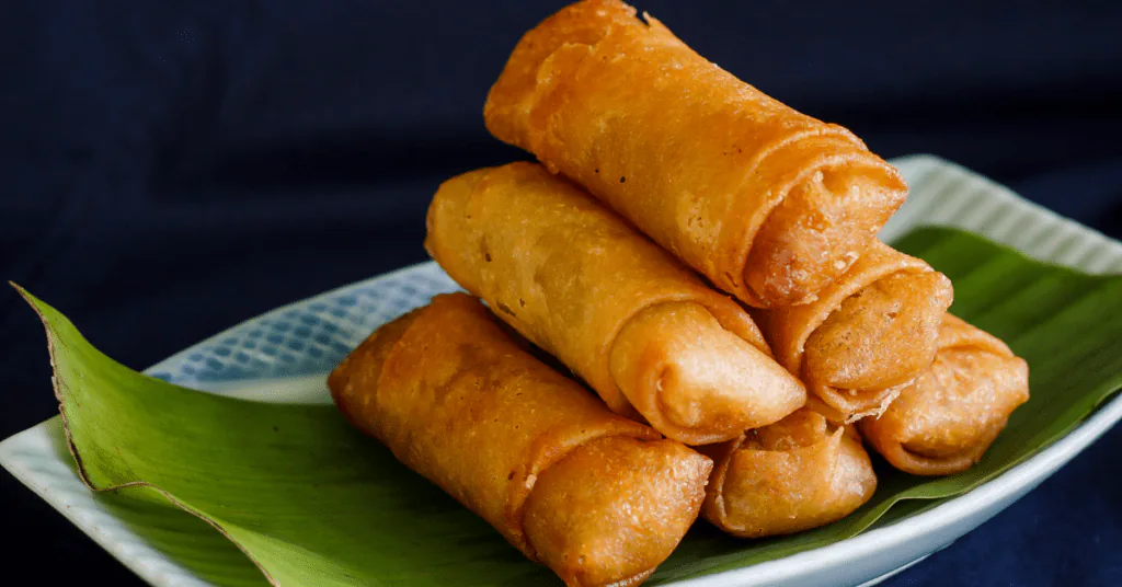 Stack of golden fried spring rolls served on a banana leaf