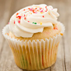 Funfetti cupcake with swirled white frosting and rainbow sprinkles on a wooden table