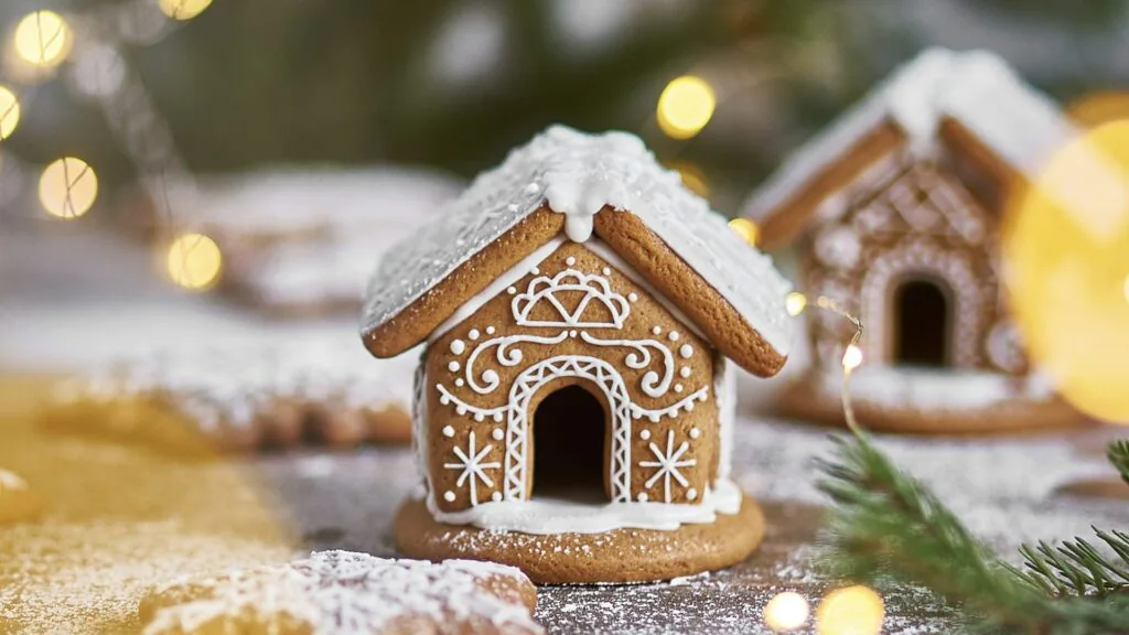 Small gingerbread houses piped with white icing and dusted with powdered sugar snow under warm lights