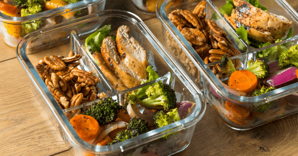 Glass meal prep containers filled with sliced chicken, roasted broccoli, carrots and pecans