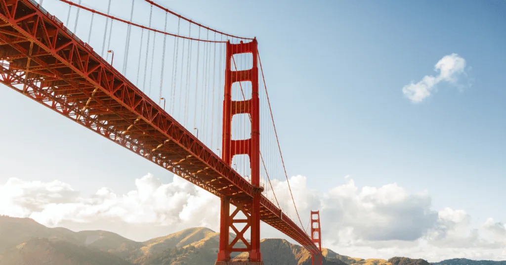 The Golden Gate Bridge seen from below, its red towers rising against a blue sky