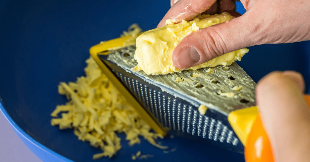 Hand grating a block of butter on a box grater into a blue bowl