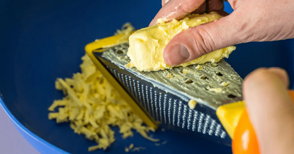 Hand grating a block of butter on a box grater into a blue bowl