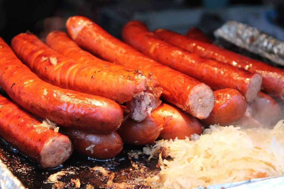 Pile of grilled bratwurst sausages next to a mound of sauerkraut on a hot griddle