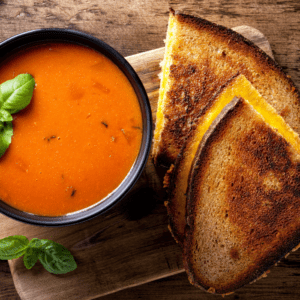 Toasted grilled cheese sandwich beside a bowl of tomato soup garnished with fresh basil
