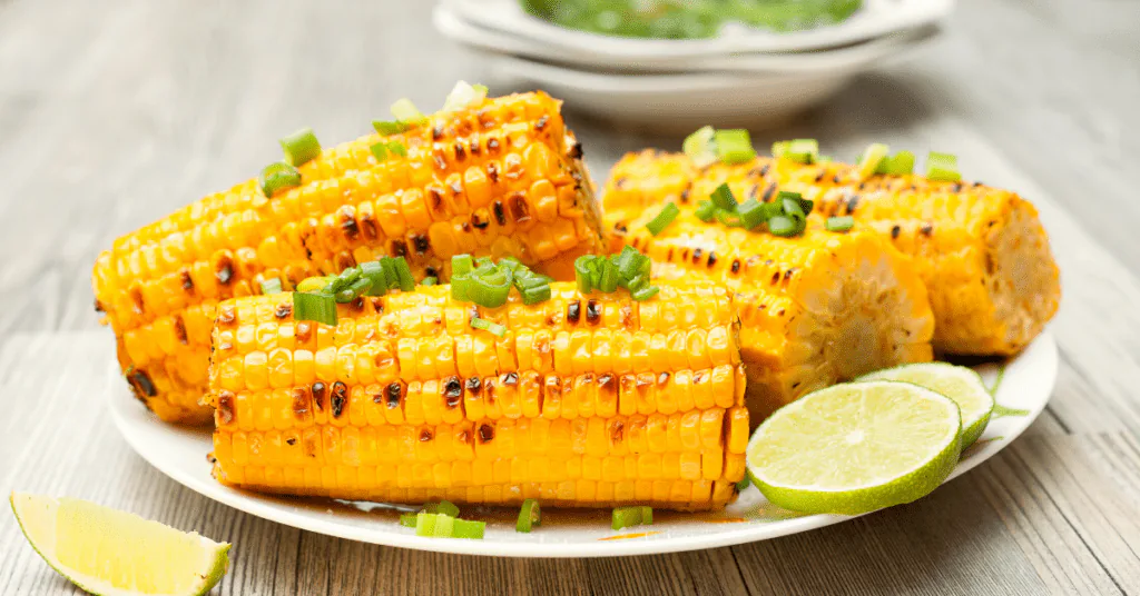 Grilled corn on the cob sprinkled with scallions and cilantro, served with lime wedges