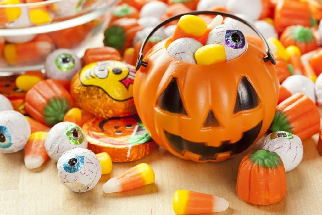 Jack-o’-lantern candy pail spilling candy corn and eyeball sweets across a table