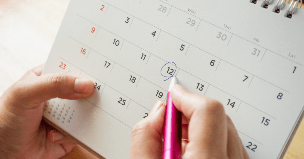 Hand circling a date on a monthly wall calendar with a pink pen