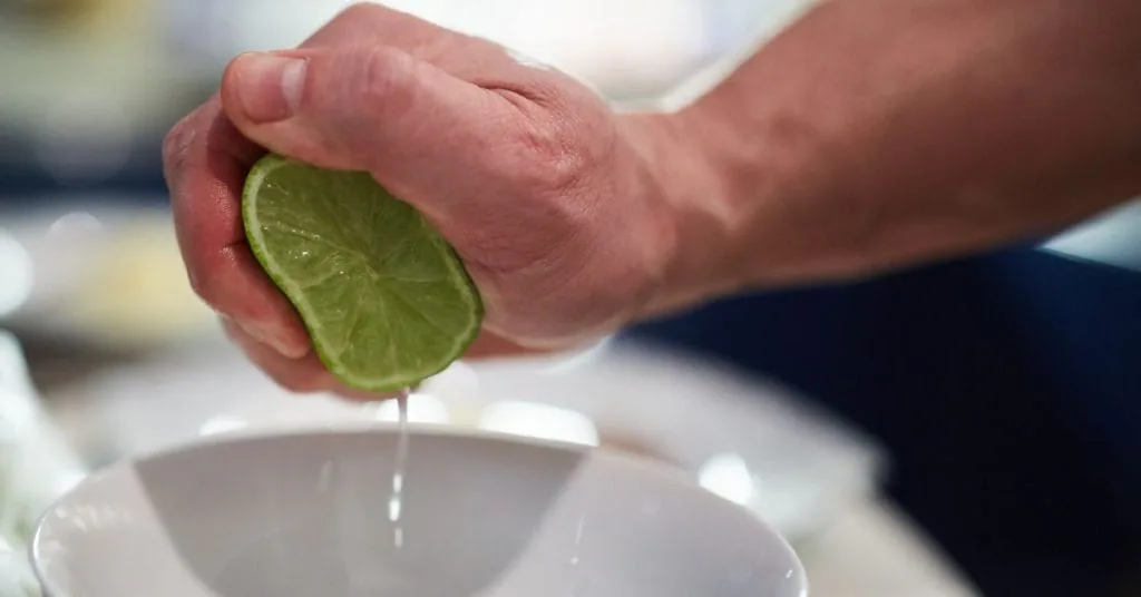 Hand squeezing juice from half a lime into a white bowl