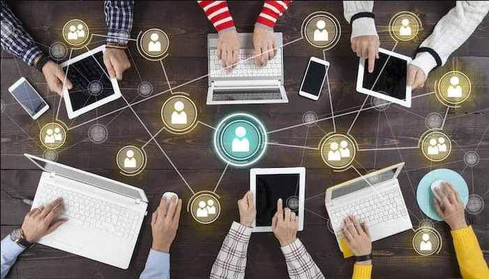 Overhead view of hands working on laptops and tablets around a table with a network graphic
