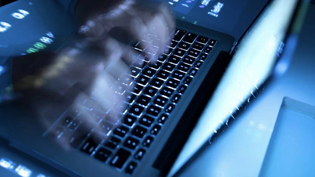 Hands typing quickly on a backlit laptop keyboard lit in blue