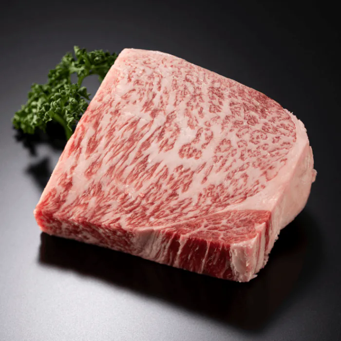Thick cut of heavily marbled raw wagyu ribeye beside a sprig of parsley on a dark surface