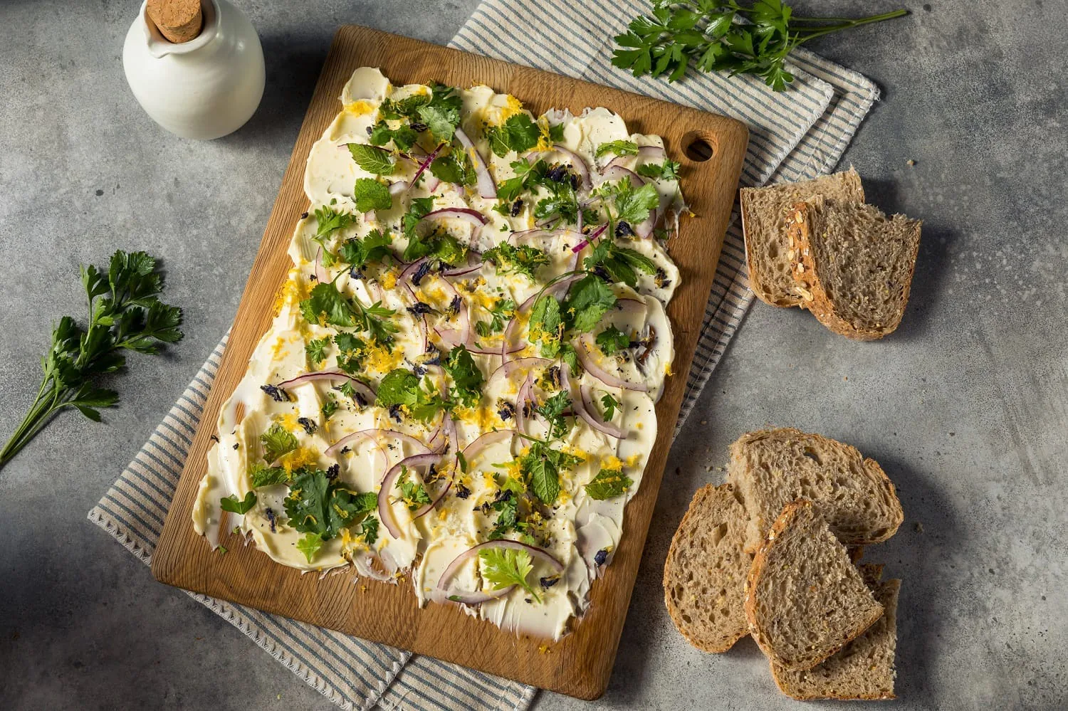 Herbed flatbread with red onion, olives and lemon zest on a wooden board beside sliced bread