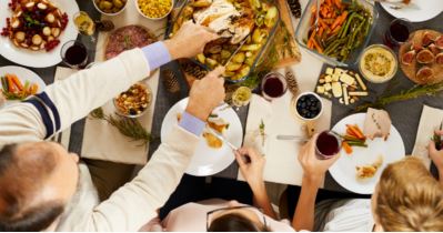 Overhead view of people around a holiday table serving roast turkey with wine and side dishes