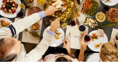 Overhead view of people around a holiday table serving roast turkey with wine and side dishes