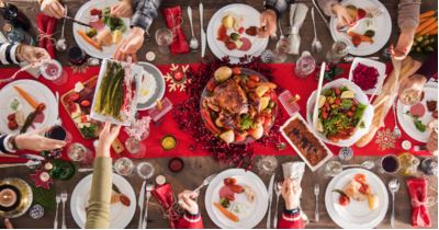 Overhead view of a festive holiday table with roast turkey, side dishes and guests reaching in