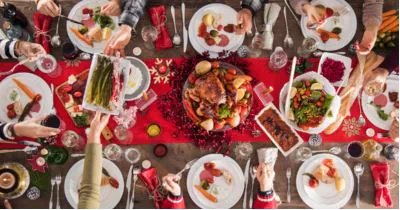 Overhead view of a festive holiday table with roast turkey, side dishes and guests reaching in