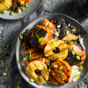 Charred huli huli chicken with grilled pineapple rings and sliced scallions served over rice