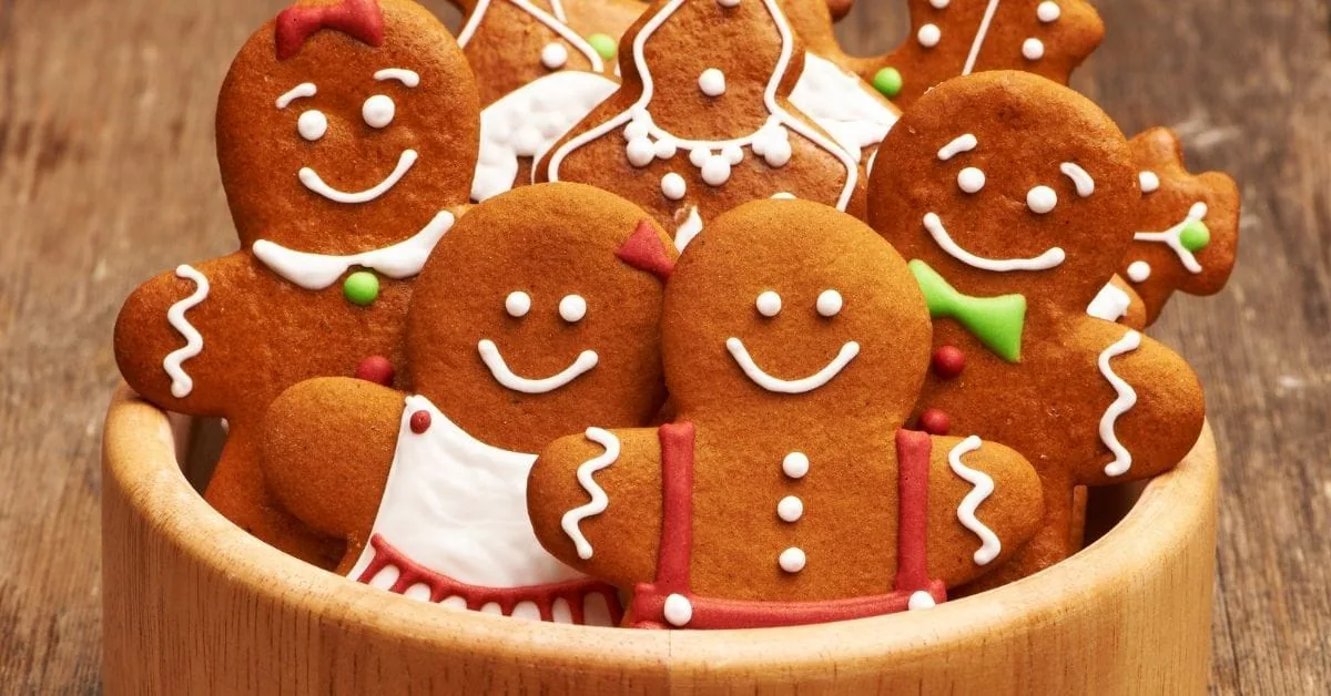 Gingerbread man cookies decorated with white icing piled in a wooden bowl