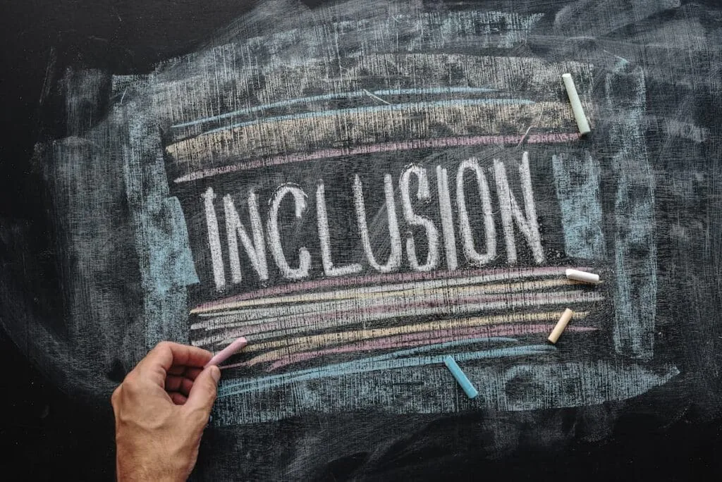 Hand writing the word Inclusion in chalk on a colourfully underlined blackboard
