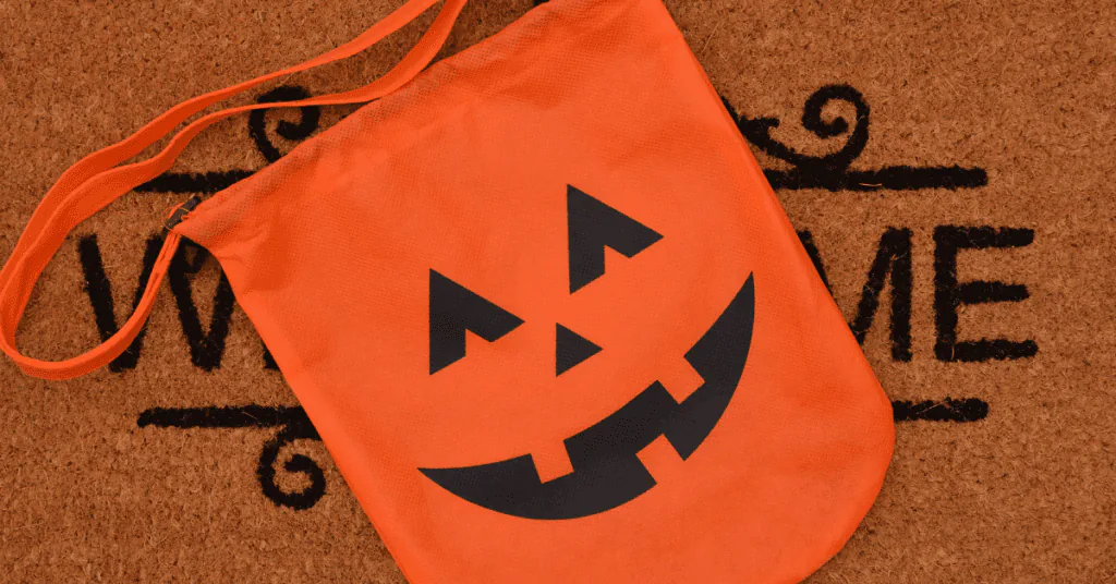 Orange jack-o’-lantern trick-or-treat tote bag lying on a Welcome doormat