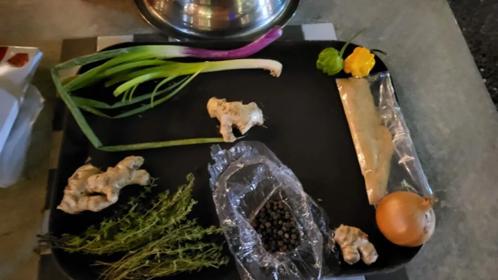 Tray of jerk chicken ingredients: scallions, fresh ginger, thyme, peppercorns and an onion