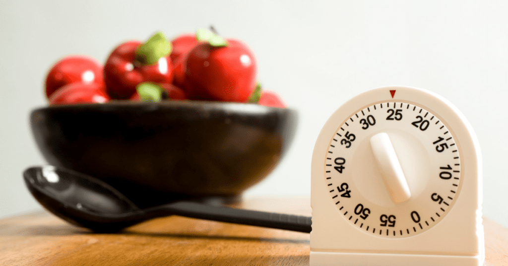 Wind-up kitchen timer set to 25 minutes next to a black ladle and a bowl of red peppers