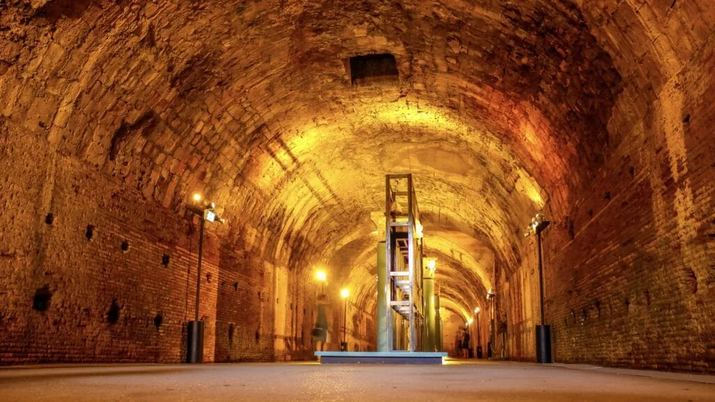 Lamplit brick barrel-vaulted tunnel stretching into the distance