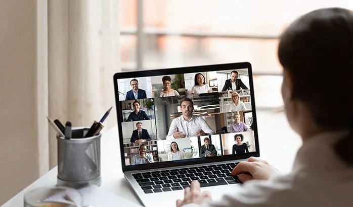 Over-the-shoulder view of a laptop video call with twelve colleagues in gallery view