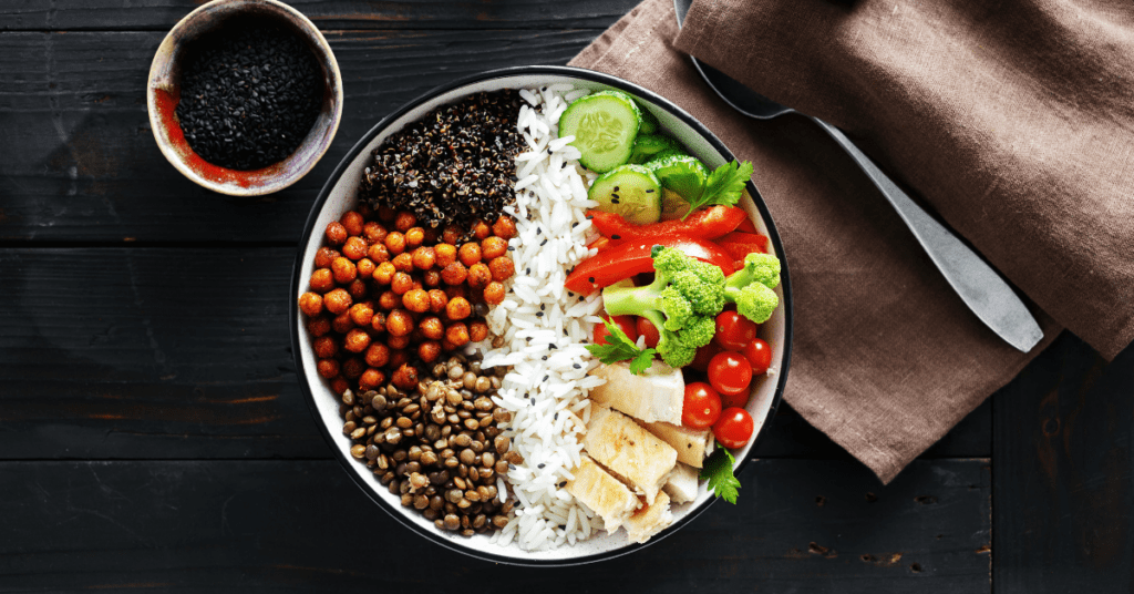 Buddha bowl of lentils, roasted chickpeas, quinoa, rice and fresh vegetables on a dark table