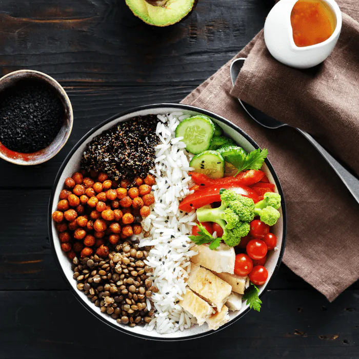 Lentil Buddha bowl with chickpeas, quinoa, rice and vegetables beside a jug of dressing