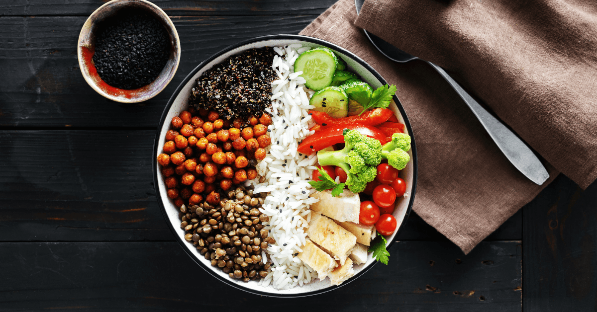 Bowl of rice with lentils, chickpeas, tofu, broccoli, tomato and cucumber on a dark wooden table