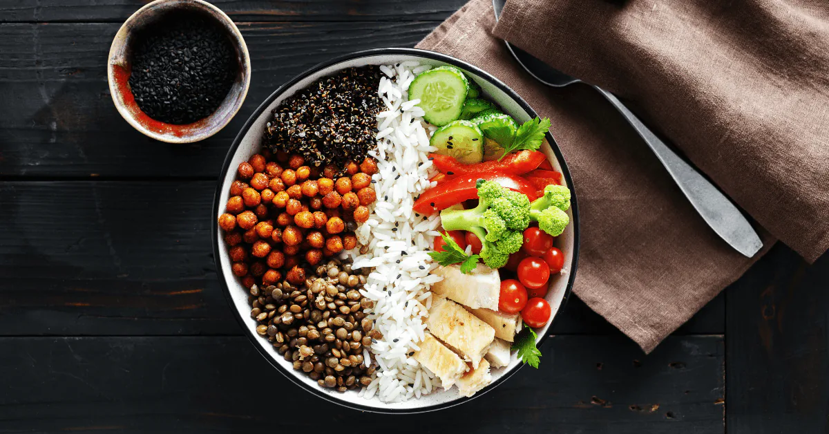 Bowl of rice with lentils, chickpeas, tofu, broccoli, tomato and cucumber on a dark wooden table