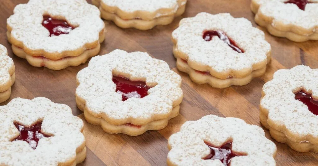 Linzer cookies dusted with powdered sugar, red jam showing through their cut-out centers