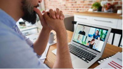 Man at a desk watching colleagues on a laptop video call from home