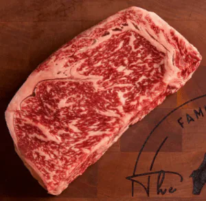 Heavily marbled raw wagyu ribeye steak resting on a wooden board
