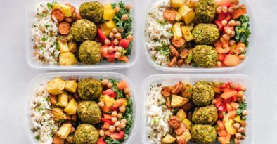 Four meal prep containers of falafel, rice, roast potatoes, chickpeas and chopped peppers