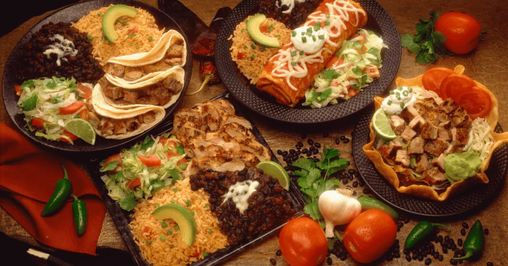 Spread of Mexican dishes including tacos, enchiladas, rice, beans and a taco salad bowl