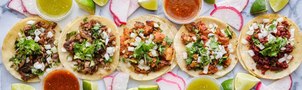 A row of Mexican street tacos with chicken, cilantro and salsa
