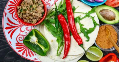 Overhead spread of tortillas, seasoned meat, red chiles, poblano, avocado and lime for Mexican cooking