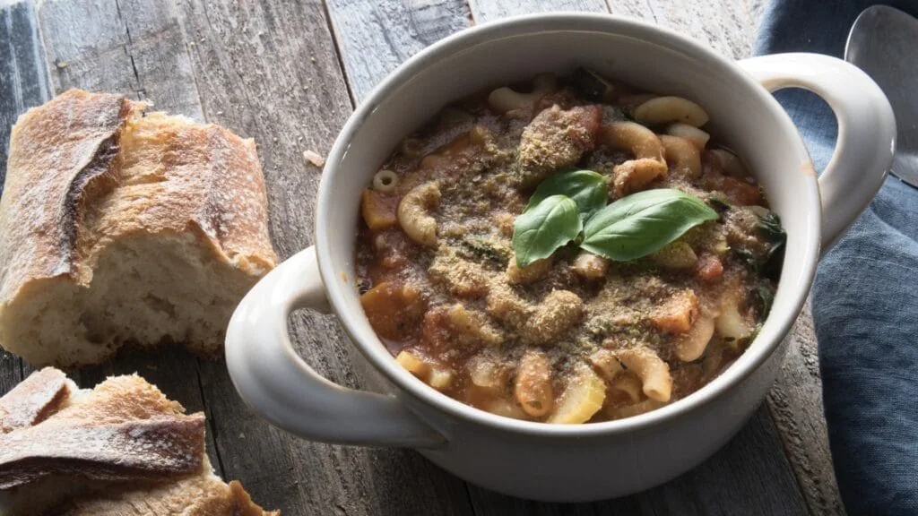 Bowl of minestrone soup topped with fresh basil beside torn crusty bread