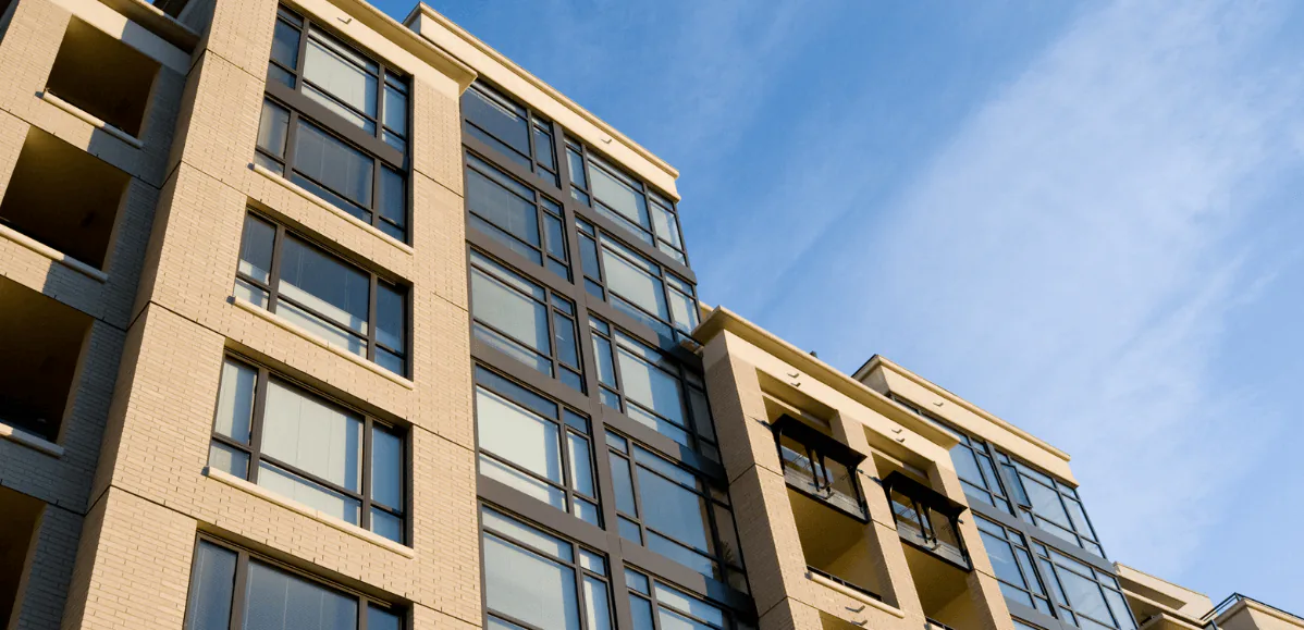 Modern condominium building with tall glass windows seen from below against a clear blue sky