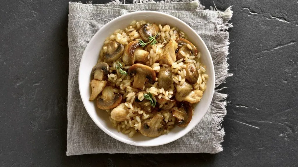 Overhead bowl of creamy mushroom risotto with thyme on a linen napkin