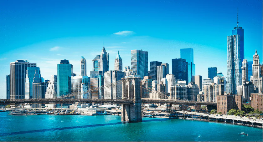 Lower Manhattan skyline rising behind the Brooklyn Bridge on a clear blue day