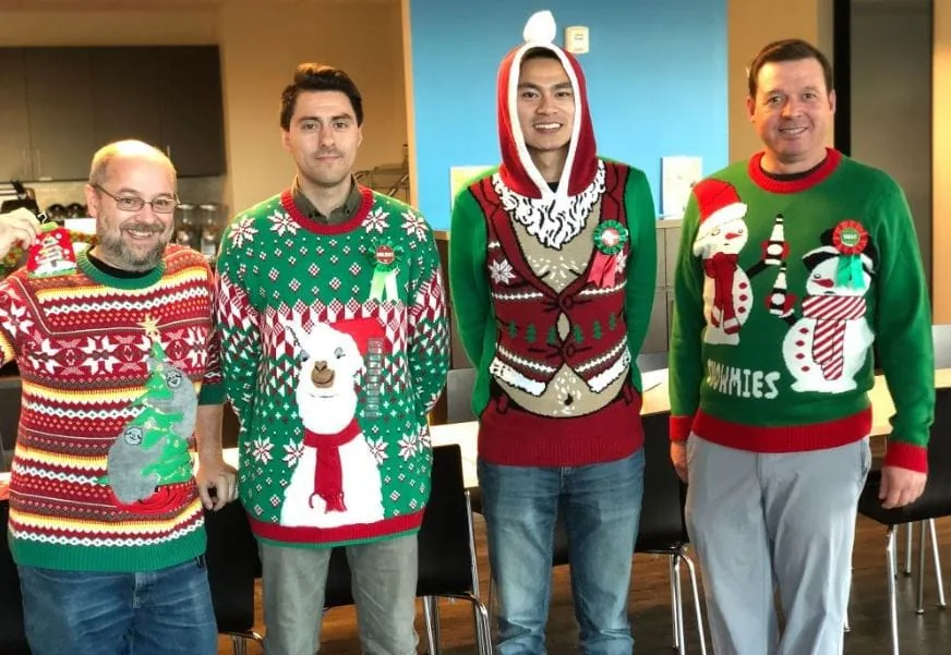 Four coworkers lined up in an office wearing ugly Christmas sweaters