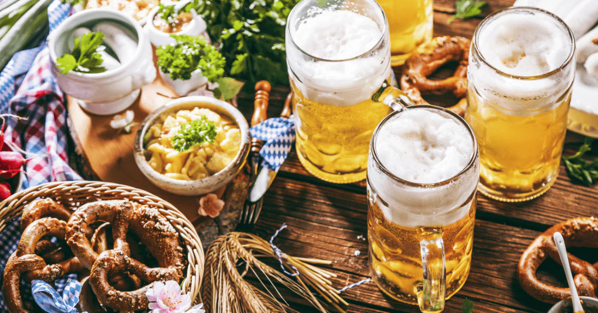Frothy beer steins on a rustic wooden table with soft pretzels, wheat stalks and blue Bavarian check linens